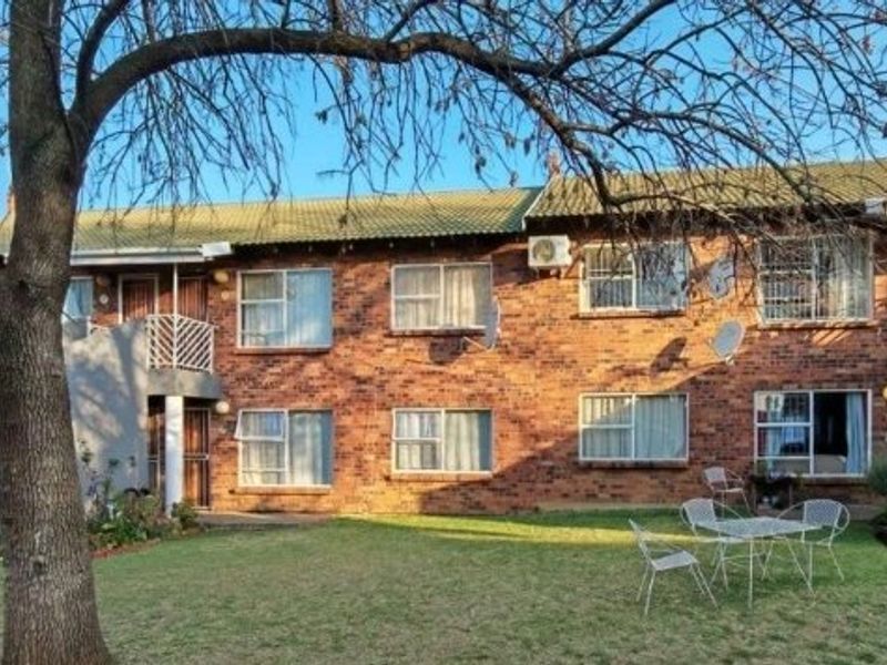 Rear view of a multi-story brick townhouse complex featuring a shared garden area, security-fitted windows, and balcony access.