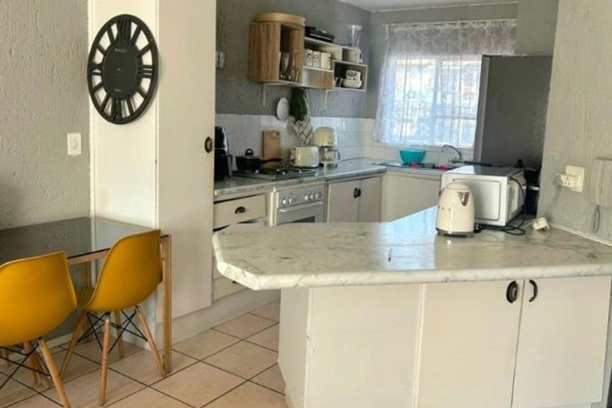 A functional kitchen featuring built-in cabinetry, laminate countertops, a tiled backsplash, and a breakfast bar area with tiled flooring.