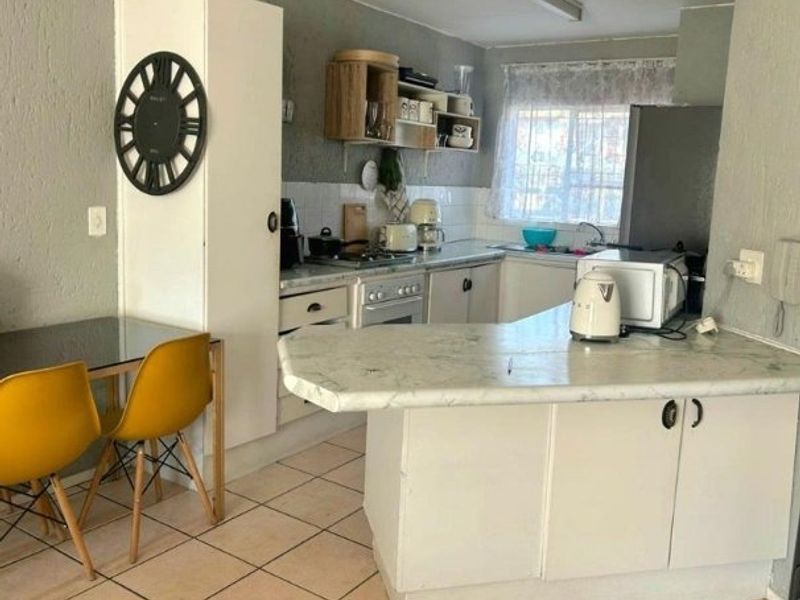 A functional kitchen featuring built-in cabinetry, laminate countertops, a tiled backsplash, and a breakfast bar area with tiled flooring.