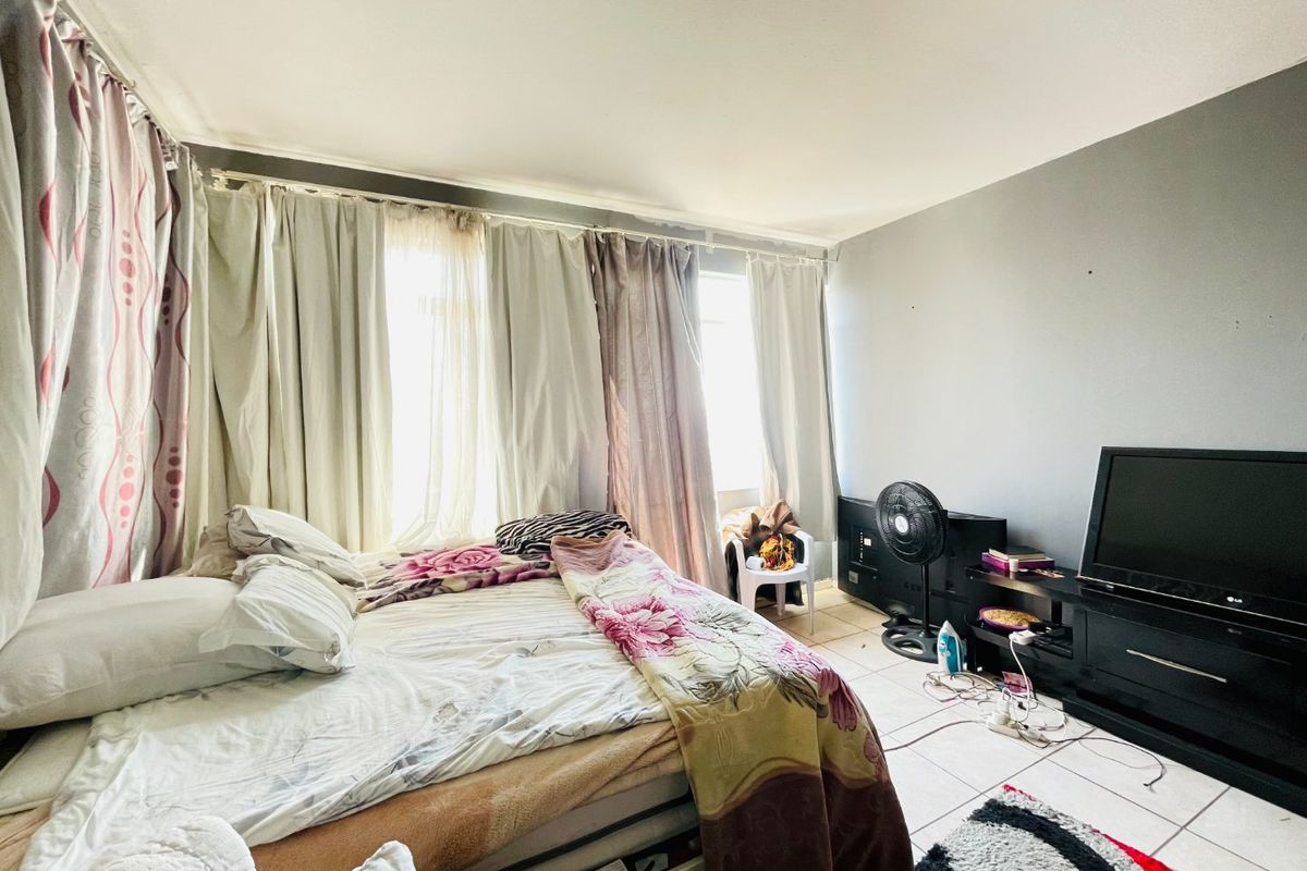 A bedroom featuring tiled flooring and large windows with curtain rails, offering a functional space with potential for cosmetic updates.