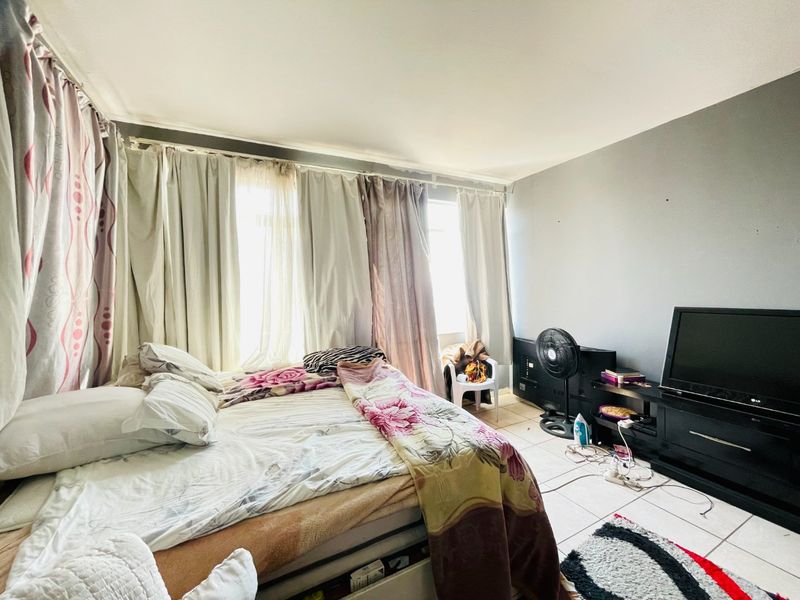 A bedroom featuring tiled flooring and large windows with curtain rails, offering a functional space with potential for cosmetic updates.