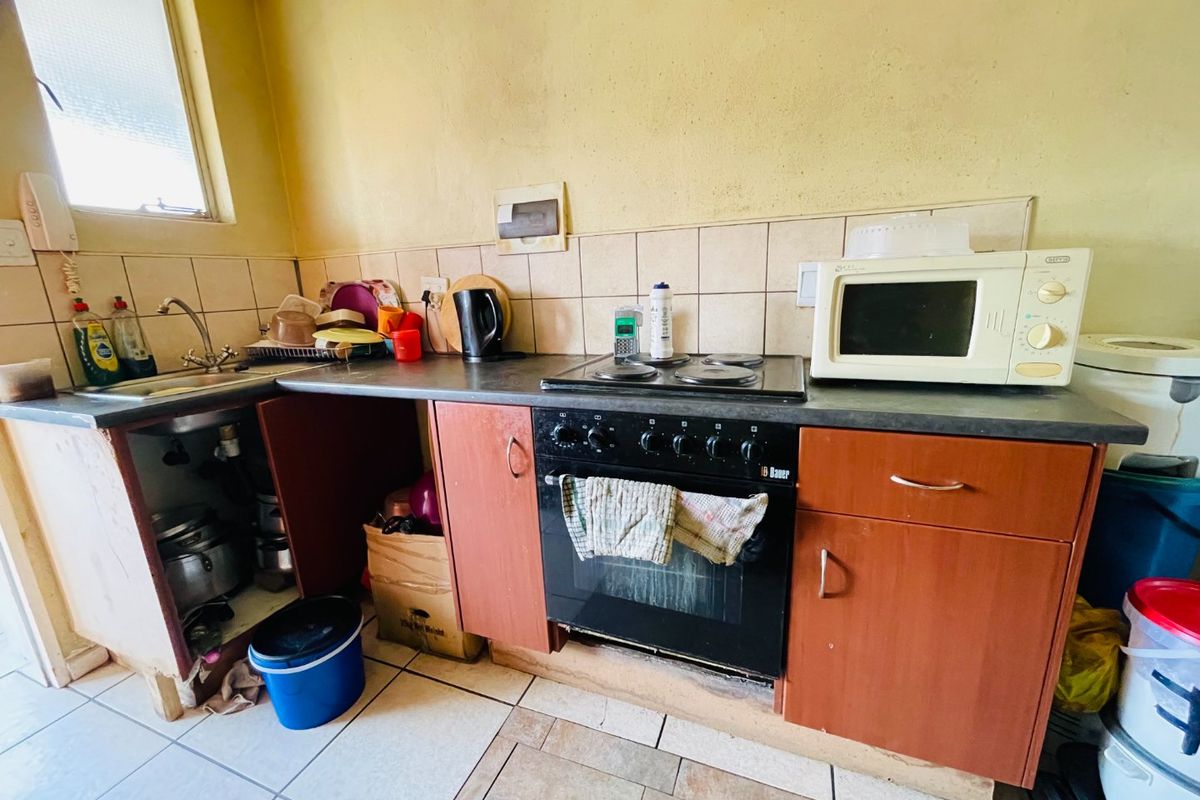 A dated kitchen featuring a built-in oven, electric hob, and sink, requiring significant cosmetic updates and repairs to cabinetry and wall finishes.