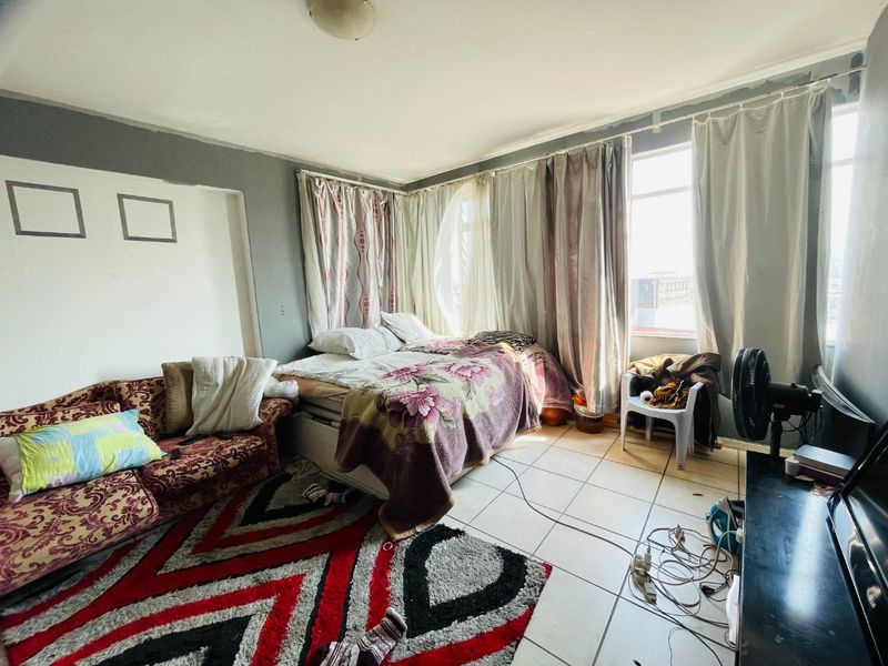 A bedroom featuring tiled flooring and large windows. The space requires cosmetic updates, including wall finishing and painting, to improve its overall appeal.