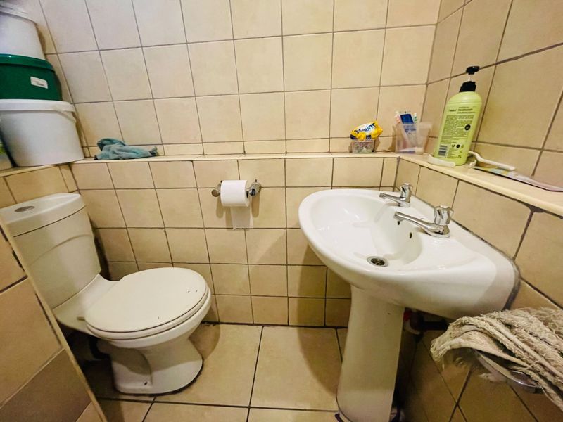 Compact bathroom featuring a pedestal basin and dual flush toilet with full-height ceramic wall tiling and tiled flooring.