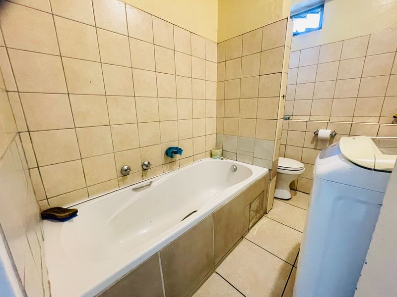 A functional bathroom featuring a built-in bathtub, ceramic tiling, and a standard toilet, offering a practical layout with potential for modernization.
