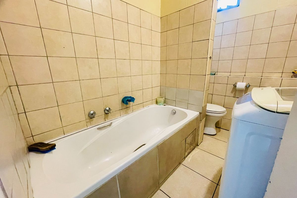 A functional bathroom featuring a bathtub with wall-mounted mixer taps, a toilet, and neutral ceramic tiling throughout.