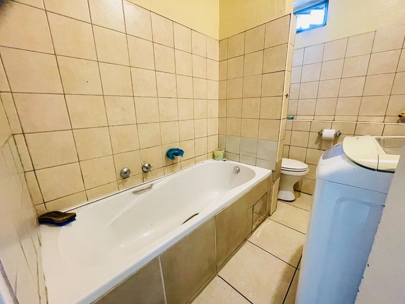 A functional bathroom featuring a bathtub with wall-mounted mixer taps, a toilet, and neutral ceramic tiling throughout.