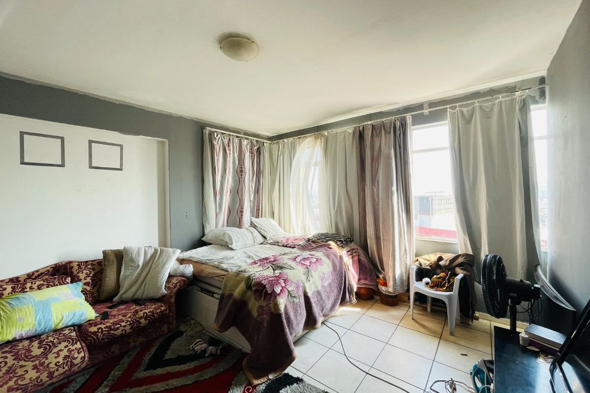 A bedroom featuring tiled flooring and large windows, currently requiring cosmetic updates to the wall finishes to improve the overall aesthetic.