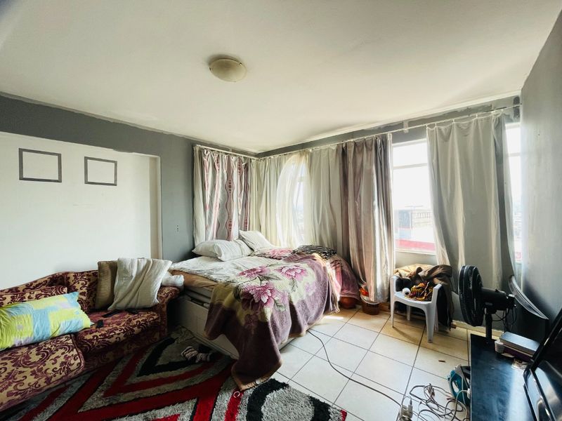A bedroom featuring tiled flooring and large windows, currently requiring cosmetic updates to the wall finishes to improve the overall aesthetic.