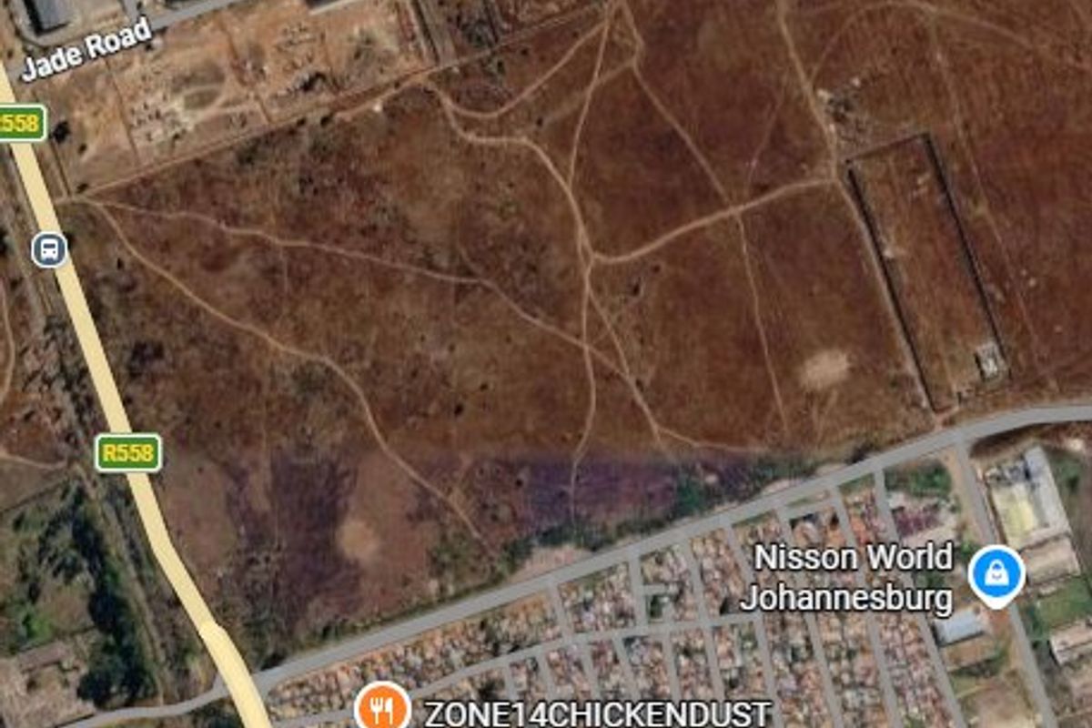 Aerial view of a large, undeveloped vacant residential plot situated near major road infrastructure and existing residential developments.