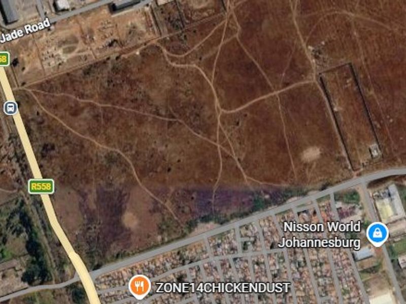 Aerial view of a large, undeveloped vacant residential plot situated near major road infrastructure and existing residential developments.