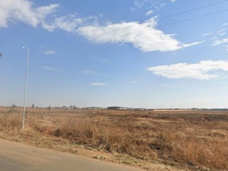 A street-level view of a large, undeveloped residential plot of land adjacent to a paved road with existing street lighting.