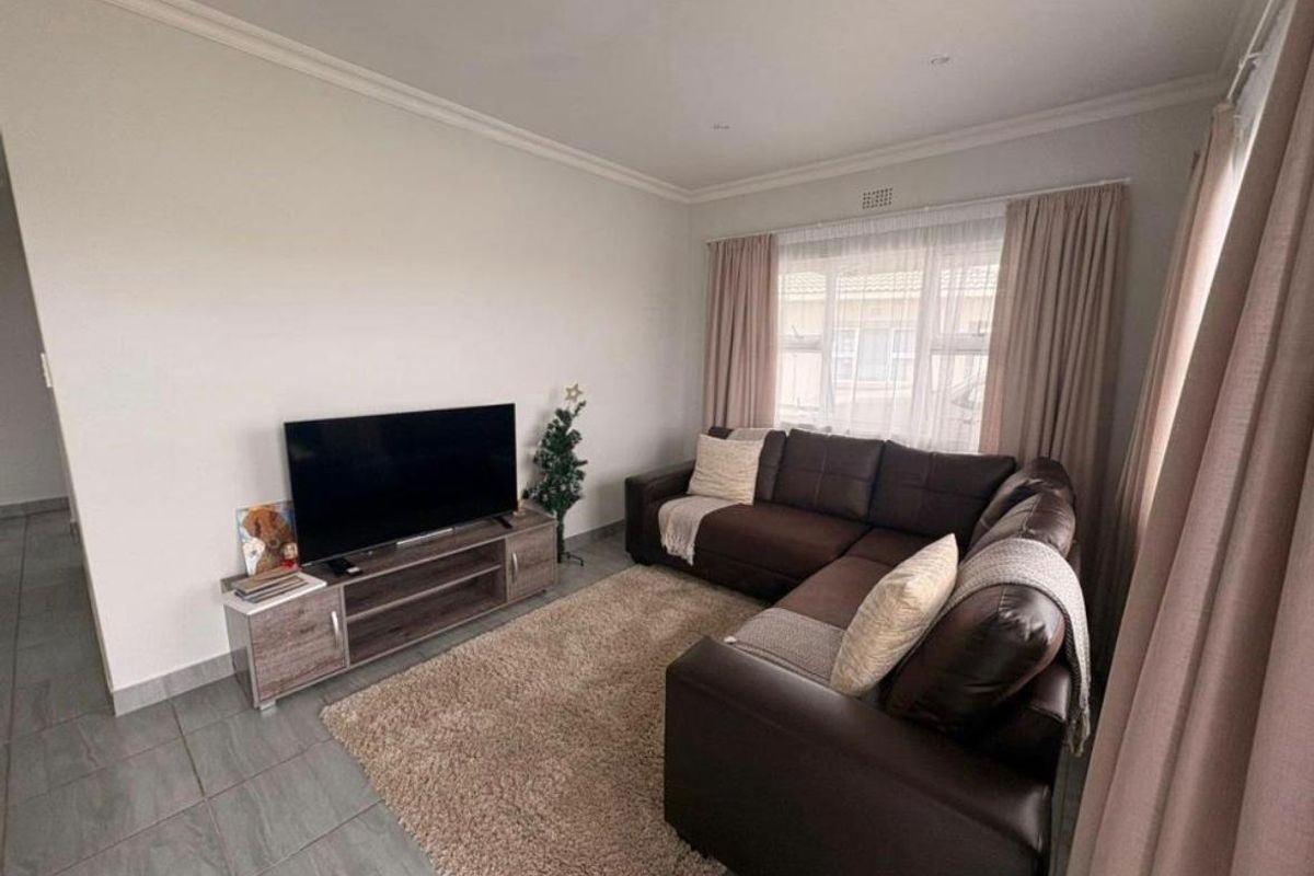 A comfortable living room featuring neutral tiled flooring, recessed downlighting, and classic cornicing, providing a clean and functional space.