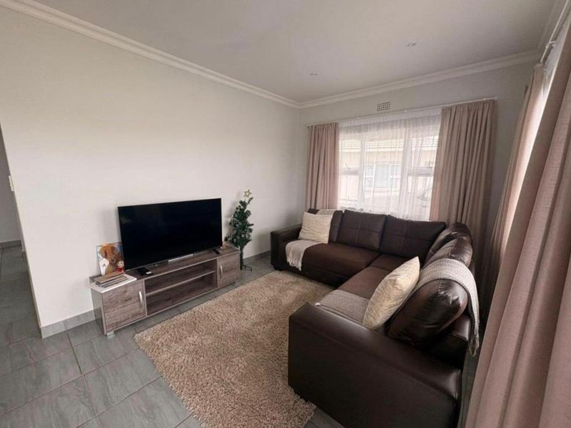 A comfortable living room featuring neutral tiled flooring, recessed downlighting, and classic cornicing, providing a clean and functional space.