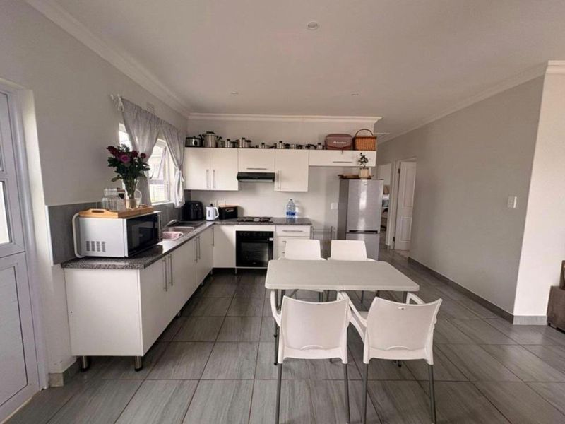 Open-plan kitchen featuring white cabinetry, built-in oven, extractor fan, and tiled flooring, seamlessly integrated with a dining area.