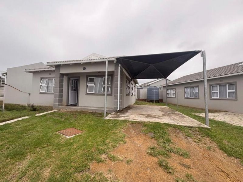 Front view of a single-story house featuring a shade sail carport, concrete driveway, and established lawn area.