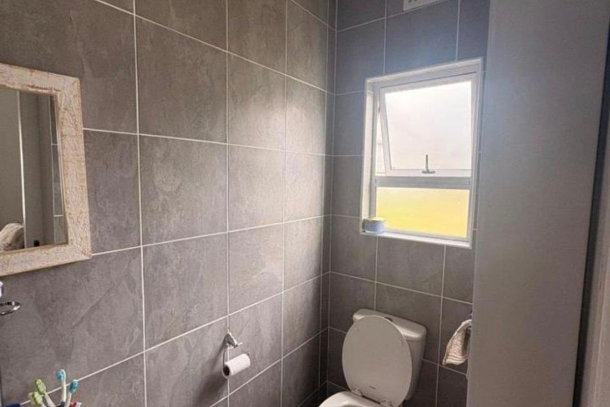 A compact bathroom featuring modern grey wall tiles, a white toilet, and a wall-mounted basin with a window for natural light and ventilation.