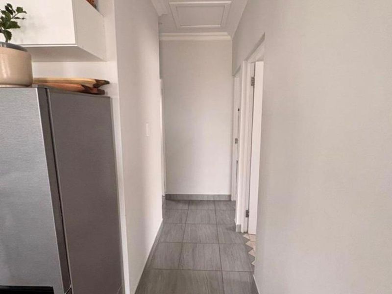 A clean, neutral hallway featuring grey tiled flooring and a ceiling access hatch, providing a functional transition space between rooms.