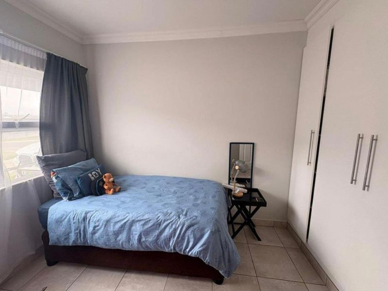 A well-maintained bedroom featuring neutral walls, tiled flooring, and a spacious built-in wardrobe.