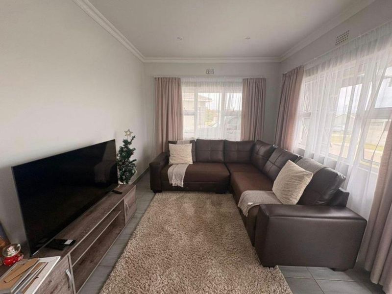 A well-maintained living room featuring neutral tiled flooring, decorative ceiling cornicing, and recessed downlighting, providing a comfortable and functional space.