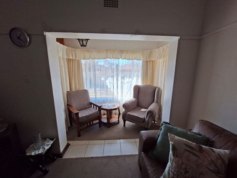 A living room area featuring a bay window with tiled flooring and visible signs of wear on the surrounding wall plaster.
