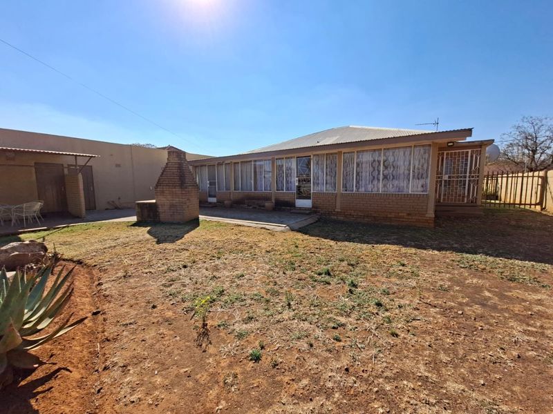 Rear view of the property featuring a paved patio area, a built-in brick braai, and a spacious garden.