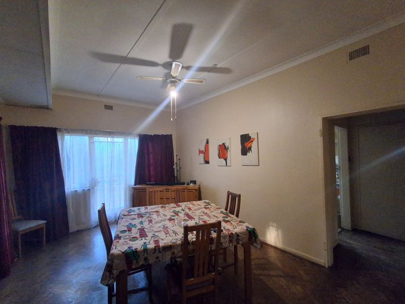 A dining room featuring classic parquet flooring, a ceiling fan, and a sliding glass door providing natural light.
