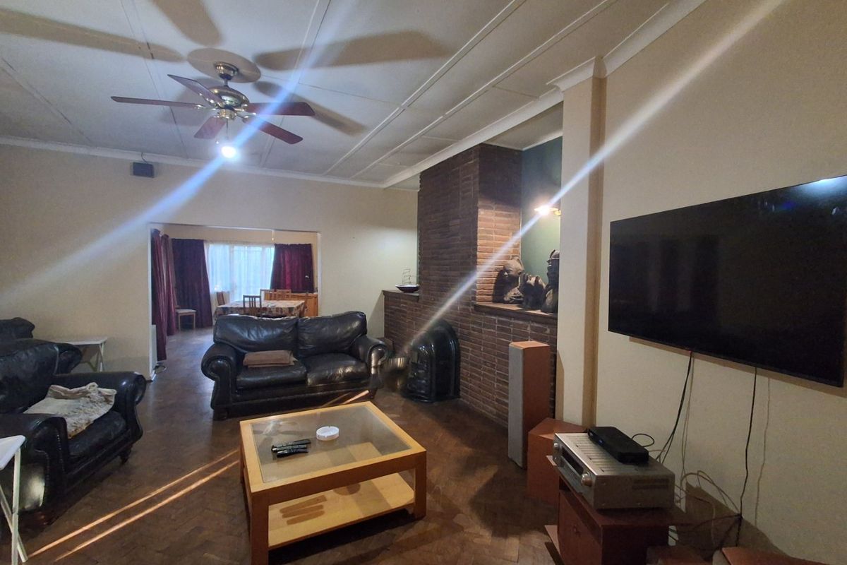 Spacious living room featuring a classic brick fireplace, parquet flooring, and a ceiling fan, offering a comfortable and traditional living space.