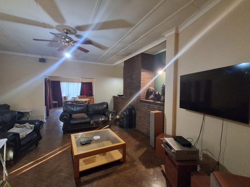 Spacious living room featuring a classic brick fireplace, parquet flooring, and a ceiling fan, offering a comfortable and traditional living space.