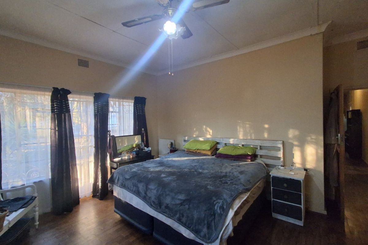 A spacious bedroom featuring parquet flooring, a ceiling fan, and large windows with security gates, offering a blank canvas for renovation.