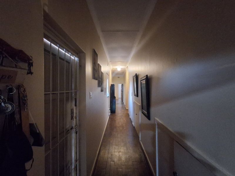 A long interior hallway featuring hardwood flooring and a security gate, providing access to various rooms within the home.