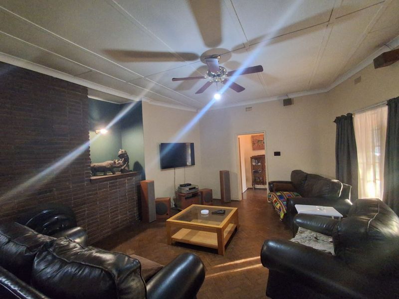 Spacious living room featuring a classic brick fireplace, traditional parquet flooring, and a ceiling fan, offering a warm and inviting atmosphere.