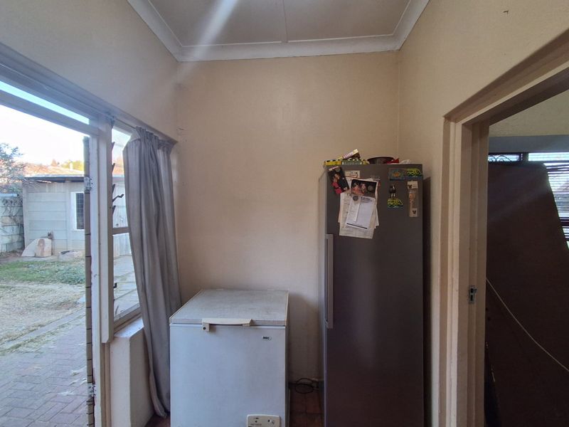 A functional scullery or utility area featuring tiled flooring, direct garden access via a sliding door, and space for refrigeration units.