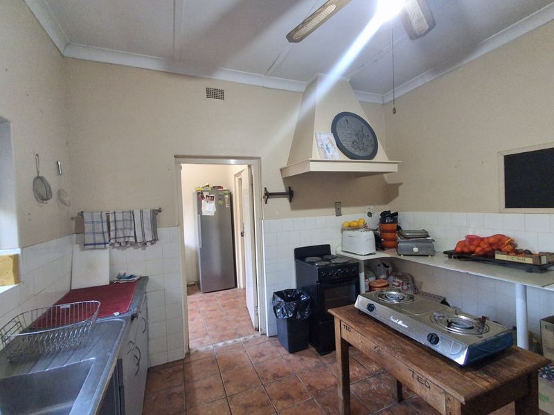 A dated kitchen featuring tiled splashbacks, a built-in extractor hood, and tiled flooring, offering significant potential for modernization and renovation.