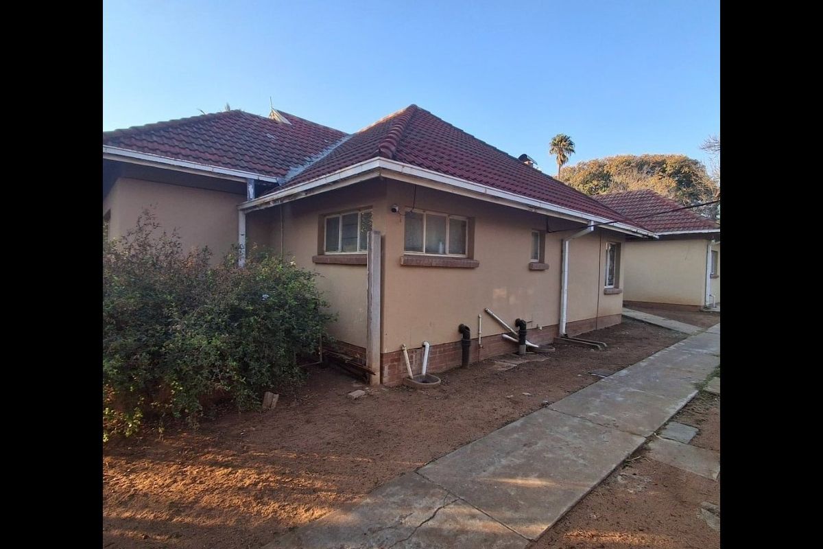Rear view of the property showing the tiled roof, exterior walls, and concrete pathway with visible plumbing infrastructure.