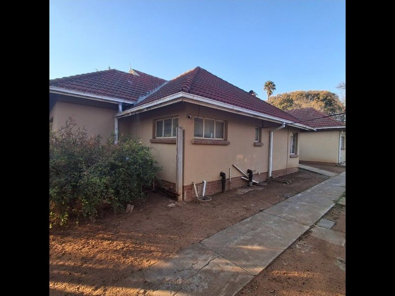 Rear view of the property showing the tiled roof, exterior walls, and concrete pathway with visible plumbing infrastructure.