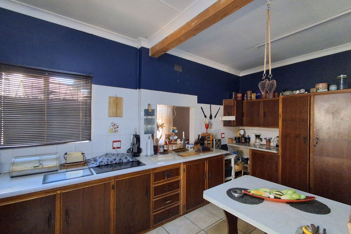 A dated kitchen featuring traditional wooden cabinetry, laminate countertops, ceramic tile backsplash, and an exposed wooden ceiling beam.