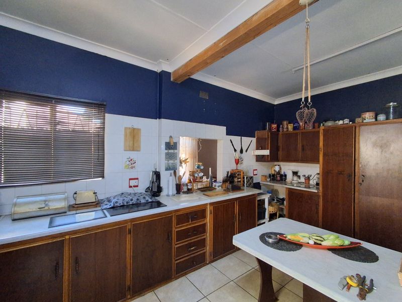 A dated kitchen featuring traditional wooden cabinetry, laminate countertops, ceramic tile backsplash, and an exposed wooden ceiling beam.