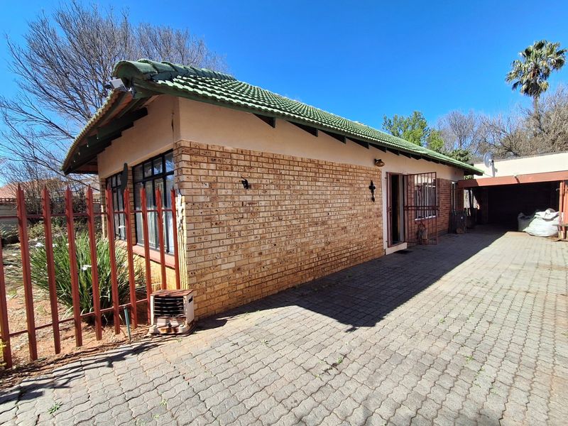 Side view of a face brick house featuring a tiled roof, paved driveway, and security gate access.