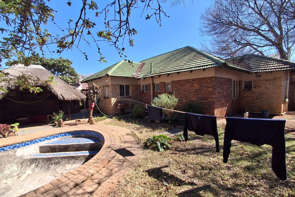 Rear view of a brick house featuring a swimming pool, a thatched lapa, and a garden area with paved surrounds.