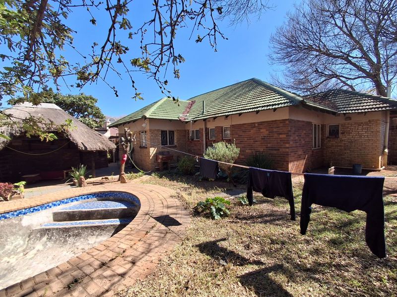 Rear view of a brick house featuring a swimming pool, a thatched lapa, and a garden area with paved surrounds.