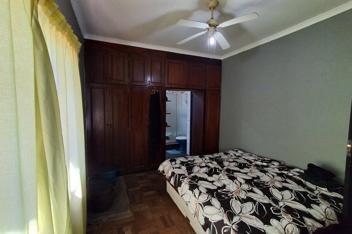 A bedroom featuring parquet flooring, built-in wooden cabinetry, and a ceiling fan, with direct access to an en-suite bathroom.