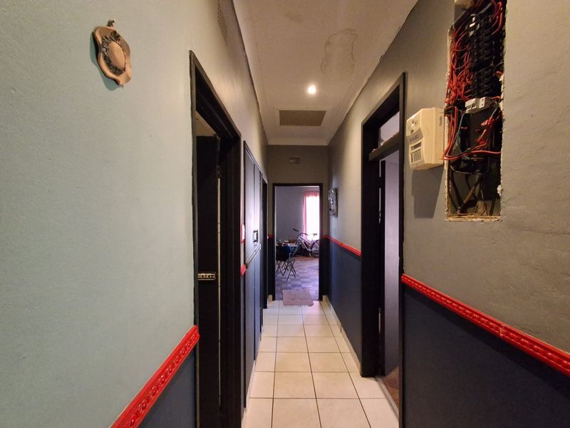 A narrow hallway featuring tiled flooring, with visible ceiling water damage and an exposed electrical distribution board requiring repair and cosmetic finishing.