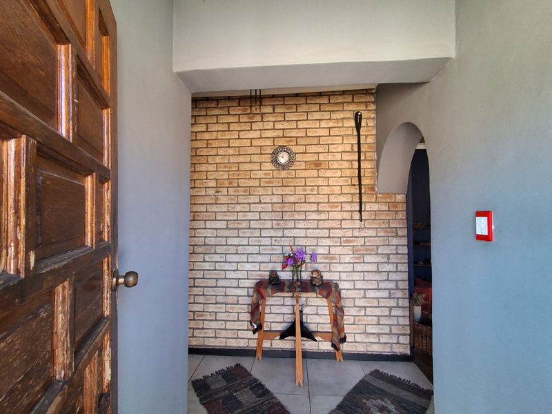 An inviting entryway featuring a rustic exposed brick feature wall, tiled flooring, and a classic solid wood entrance door with an arched transition.