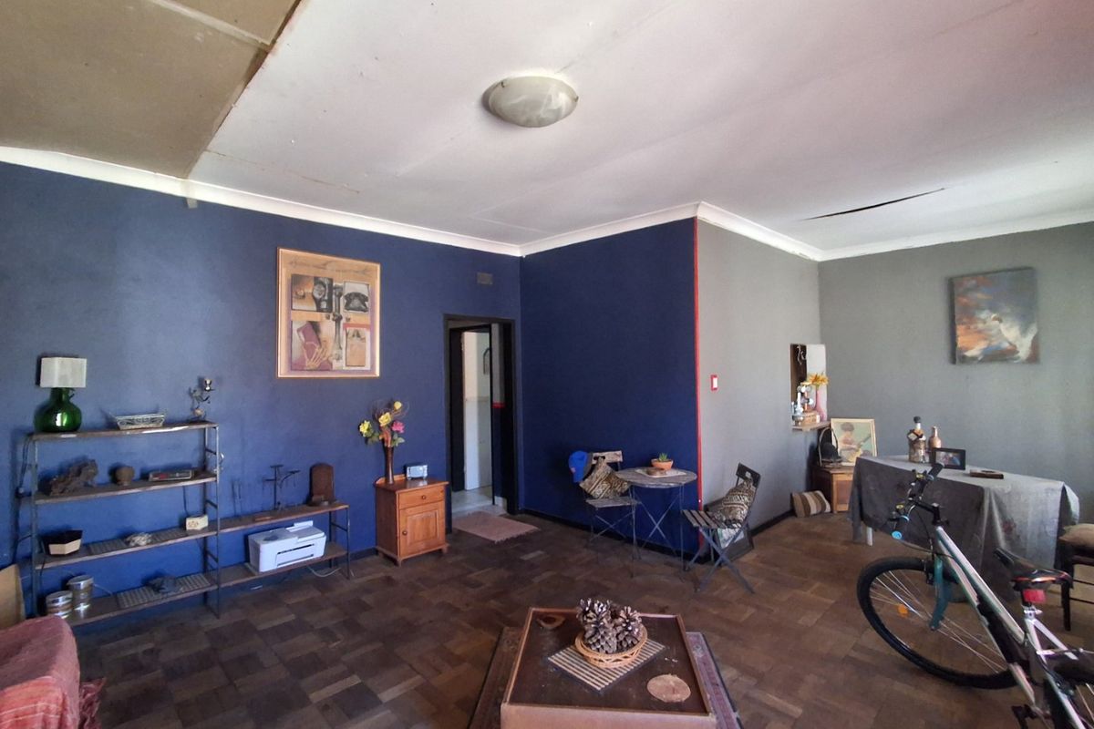 Spacious living area featuring original parquet flooring and a ceiling light fixture, requiring some cosmetic attention to the ceiling and wall finishes.