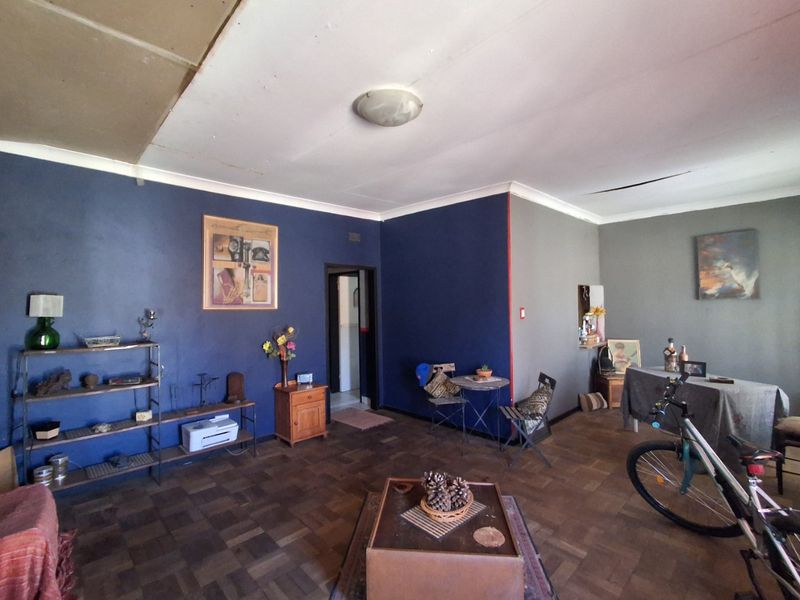 Spacious living area featuring original parquet flooring and a ceiling light fixture, requiring some cosmetic attention to the ceiling and wall finishes.