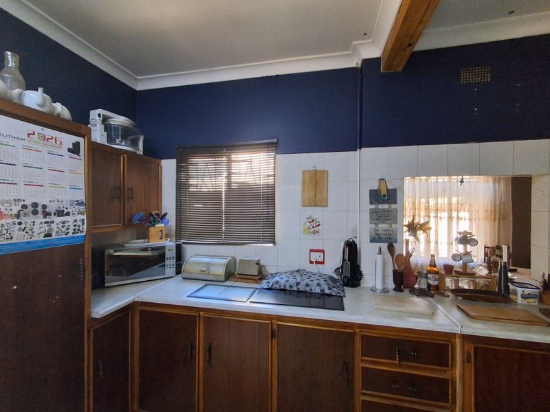 A functional kitchen featuring dark wood cabinetry, laminate countertops, a tiled backsplash, and an integrated electric hob with a pass-through window.