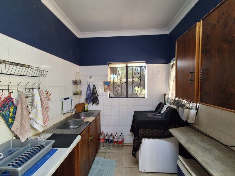 A functional laundry area featuring built-in wooden cabinetry, a double stainless steel sink, and tiled splashbacks with security bars on the window.