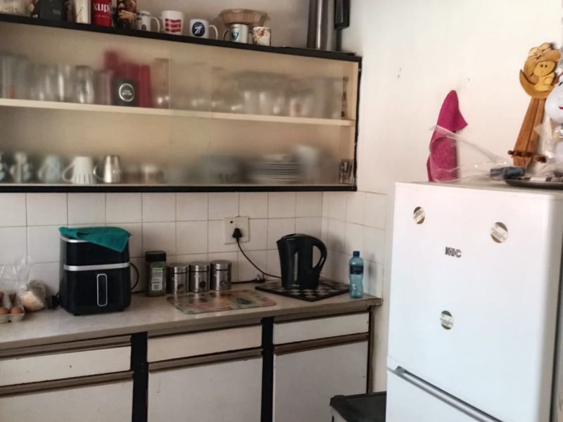 A compact kitchen area featuring dated white cabinetry, tiled backsplash, and exposed timber ceiling beams, offering potential for a modern renovation.