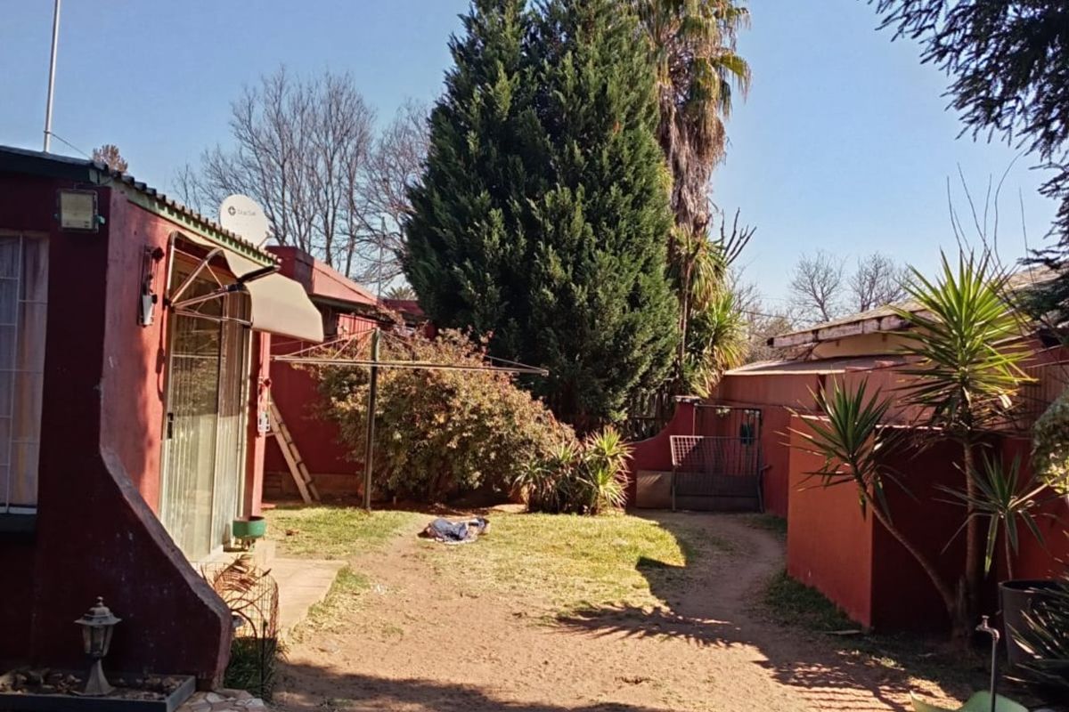 Rear exterior view of the property featuring a garden area, paved patio section, and established trees with red-painted exterior walls.